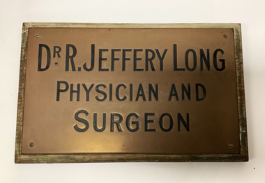 Rectangular brass name plate for Dr R. Jeffrey Long. Brass plate fixed onto a back board for mounting onto a fence. Lettering filled in in black.