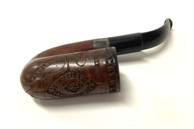 Wooden tobacco pipe with Boer War-related carved inscriptions around a central lozenge shape on the pipe bowl and on the sides of the bowl. The bowl is curved in Full-Bent Billiard style with a sterling silver collar and a vulcanite mouthpiece.