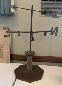 Large metal weather vane on a wooden pole, showing the four points of the compass and an arrow on the top to show wind direction. 
