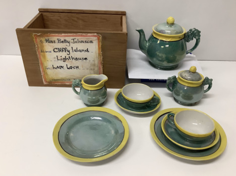 Child's Japanese ceramic tea set in a plywood box, green with yellow and black decoration on the rims of the articles. Comprising a teapot and lid. a sugar bowl and lid, a milk jug, two cups and saucers and two side plates. 