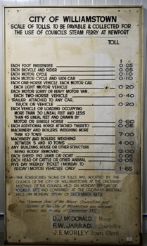 Lare white enamelled board with black print listing tolls and fares in dollars and cents for vehicles and animals for the Williamstown/Newport to Port Melbourne steam ferry. The tolls have been changed over time, and are overwitten with new fares.