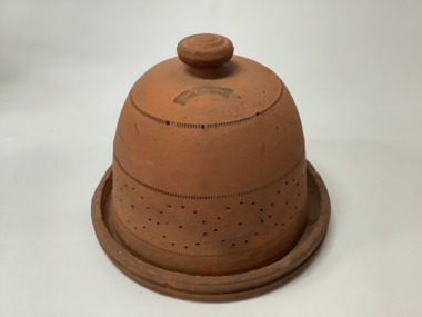 Terracotta dome shaped butter cooler with ventilation holes, designed to keep butter cool without refrigeration. Circular lifting knob. Dome sits on a terracotta base. 