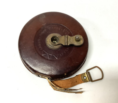 A vintage Rabone tape measure in a brown leather case with a brass winding handle.The tape has a length of 66 feet . One side of the tape is marked in inches and the reverse side is marked in links