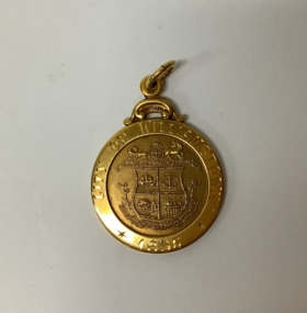Small 9 carat gold round gold medallion with ring for attaching to a chain or fob. Coat of arms of Williamstown on the face.  Obverse engraved. Commemorating Councillor R A E Ducrow, Mayor of Williamstown from 1948 to 1960. In original cream coloured plastic, square lidded box with burgundy velvet lining.