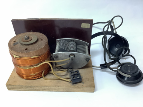 Vintage crystal radio set, home made, on a wooden stand; consisting of a coil (inductor); a tuning capacitor for selection of AM radio stations; headphones manufactured in Japan in the 1950's.