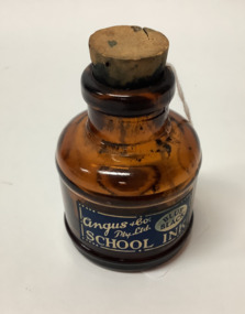 'School' brand ink bottle, made by Angus and Co. Amber coloured glass with a dark blue label, and a cork stopper.