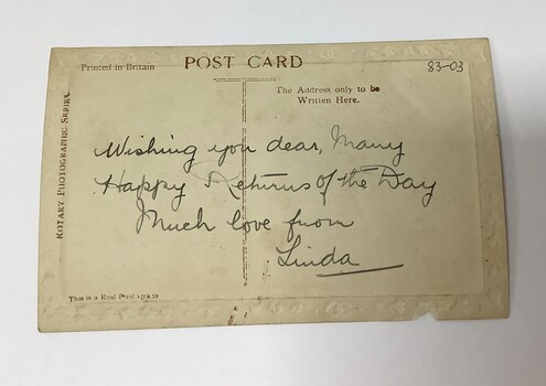 Embossed birthday card (circa 1917) on photographic paper. Decorated with flowers in the upper and lower left, and a bow and heart shape containing a small sailing yacht on the sea. 