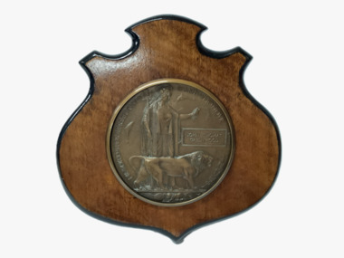 A WW1 British Empire bronze memorial plaque mounted on a timber shield awarded to John Thomas Greenwood.