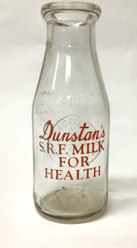 Small glass milk bottle from Dunstans Dairy Williamstown with embossed inscription and red lettering.