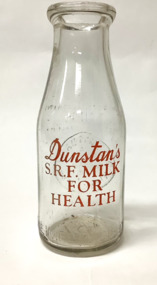Small glass milk bottle from Dunstans Dairy Williamstown with embossed inscription and red lettering.