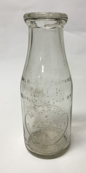 Small, clear glass milk bottle with front and back embossed inscriptions, originating from the Harney dairy in Williamstown.