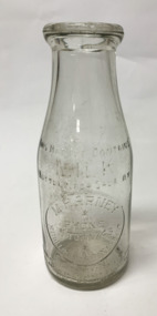 Small, clear glass milk bottle with front and back embossed inscriptions, originating from the Harney dairy in Williamstown.