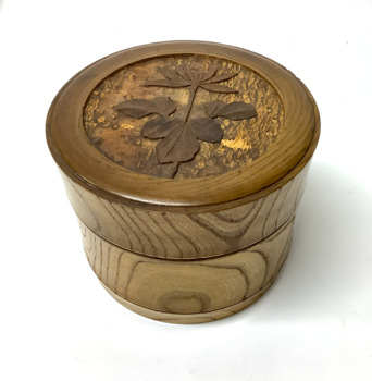 Circular lidded wooden box used to store vintage men's collars. The wood grain indicates that the was carved from a log of wood. A large flower with a stem and leaves is carved into the top of the lid.