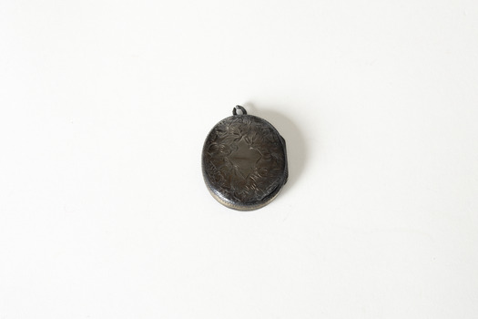 A small dark metal locket, closed, with leaf and vine decoration. 