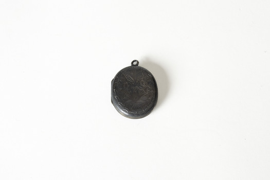 A small dark metal locket, closed, with leaf and vine decoration. 