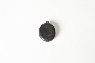 A small dark metal locket, closed, with leaf and vine decoration. 