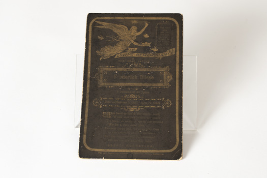 Small brown card with writing in a shade of gold. There is an angel in the top left corner, the name Frederick Buse in the center with a decorative boarder around the name and passages from the bible in the top right corner and under his name and information