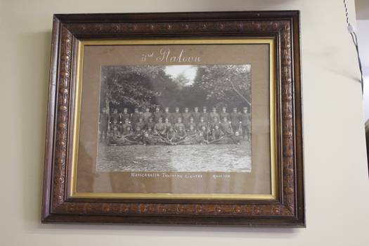 Carved timber frame containing photograph of a platoon of standing and seated WW1 soldiers.