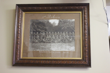 Carved timber frame containing photograph of a platoon of standing and seated WW1 soldiers.