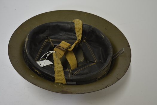 Khaki painted steel metal hat with dark brown leather and plastic coated canvas inserts, with pale khaki cloth chin strap