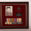 Brown timber frame with maroon velvet mount  containing 8 medals, black and white photograph, two brass badges and a black plaque with white inscription .
