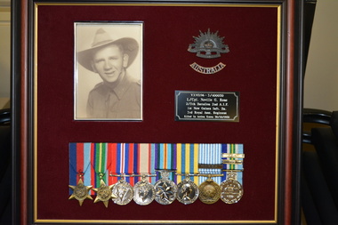 Timber frame with maroon felt mount containing photograph of soldier, eight medals with attached ribbons two metal badges and plaque.