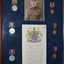 Brown timber frame with dark blue background containing photograph of soldier,  three round and three star shaped medals and document with coloured crest.