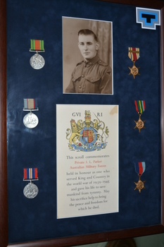 Brown timber frame with dark blue background containing photograph of soldier,  three round and three star shaped medals and document with coloured crest.