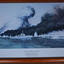 Brown timber frame containing blue black and white print of ships being bombed.