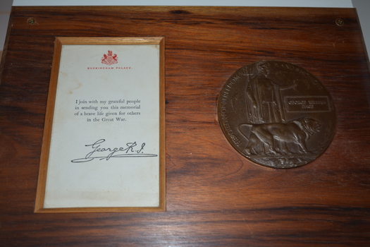 Round metal  plaque and letter with red crest mounted on rectangular timber board.