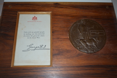 Round metal  plaque and letter with red crest mounted on rectangular timber board.