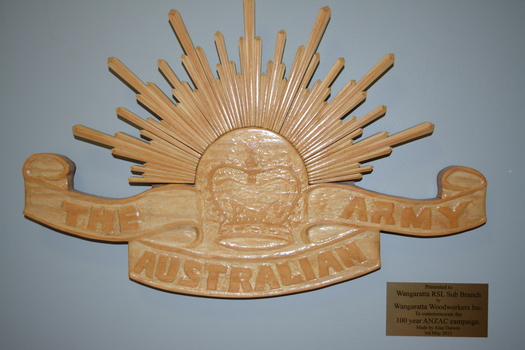 Carved timber emblem in the shape of the Rising Sun above crown and scroll