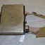 Black metal box with silver metal flap top cover affixed with  rotating circular rule .  Two  adjustable belts are affixed to the base of  black box.   
 
 