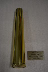 Brass shell casing 40 mm.  and gold coloured plaque with black writing.
