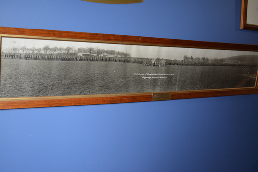 Brown timber frame containing photograph of large group of soldiers and band members in an open field.