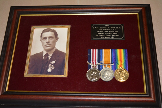 Brown timber frame with maroon felt mount containing photograph,three medals with ribbons and metal plaque