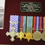 Brown timber frame containing 5 metal medals, photograph of Airman, flying patch and plague on red felt background