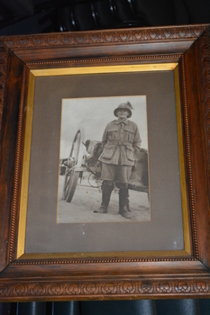 Ornate dark timber frame housing photograph of soldier wearing pith style helmet with plum standing in front of large two wheel cart/dray