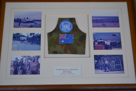 brown timber frame with off white mount containing six photographs and camouflage lanyard