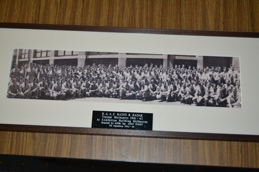 Long narrow black and white photograph of large group of airmen kneeling and standing in front of building