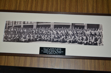 Long narrow black and white photograph of large group of airmen kneeling and standing in front of building