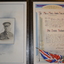 Black leather bound folder with gold coloured writing in centre front of border.  Folder contains a tribute document and photograph of soldier.