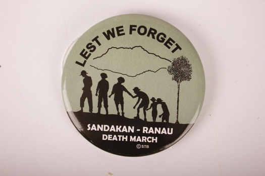 Circular badge with green background and black text and figures.  Six soldiers are silhouetted next to a tree.