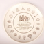 Round white ceramic plate with various royal, imperial and military gold emblems bordering an image of a brown building.