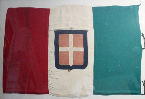 Large Italian flag with green, white and red vertical panels of equal size defaced with the Savoyan coat of arms, a red shield with white cross bordered with blue.  Three two-piece hoist ties on the green side. 