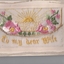 White rectangular postcard with embroidered pink flower, green foliate and yellow rising sun decoration on front.  