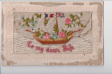 White rectangular postcard with embroidered sailing boat with flying french flag and union jack.  Also pink, blue flowers and green foliate decoration on front. 