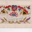 White rectangular postcard with embroidered flowers and green foliate decoration on front. 