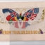 White rectangular postcard with embroidered butterfly representing the flags and colours of different countries. 