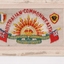 White rectangular postcard with embroidered yellow, orange, red, white rising sun badge, green banner and english maritime flags.